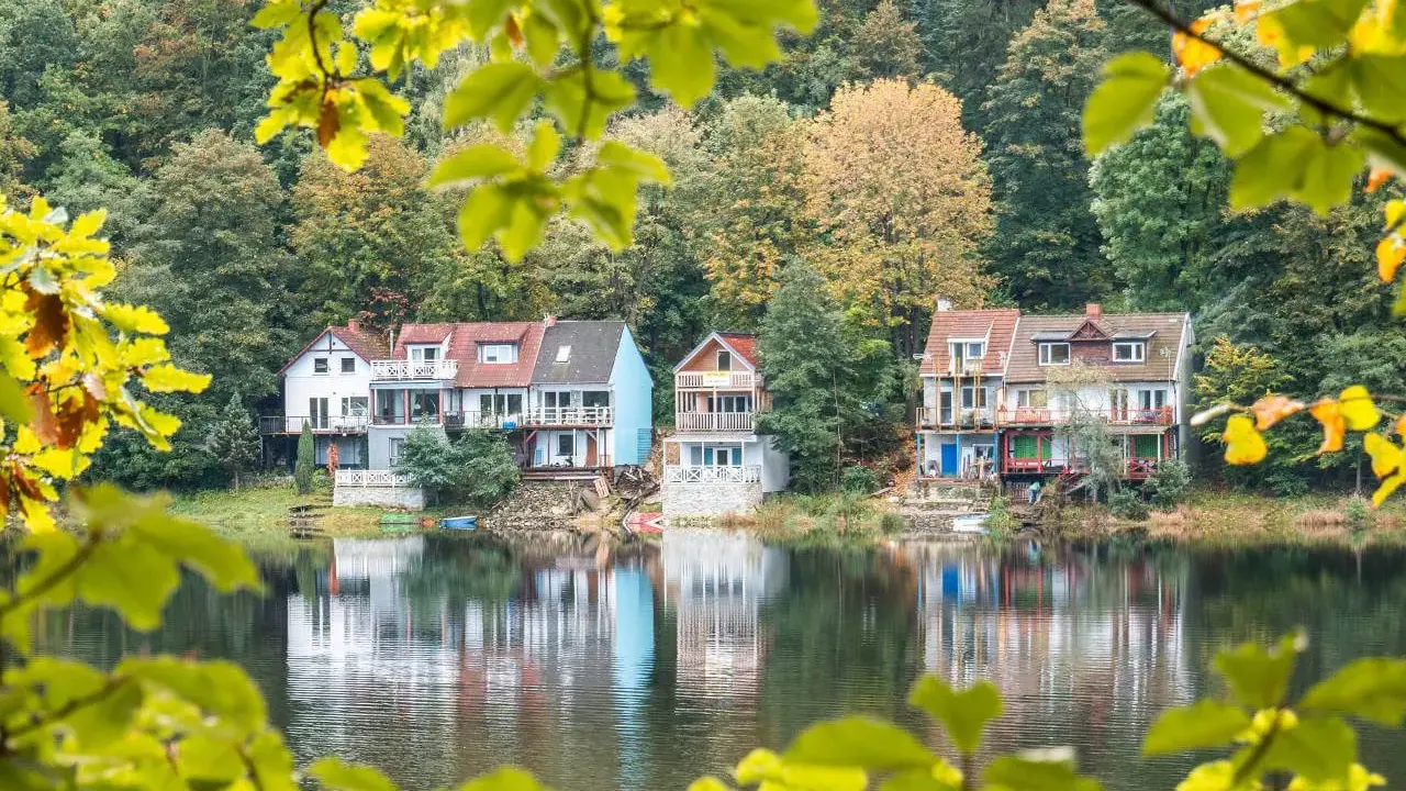 Malownicze domy nad jeziorem w okolicach Wrocławia, otoczone jesiennym lasem.