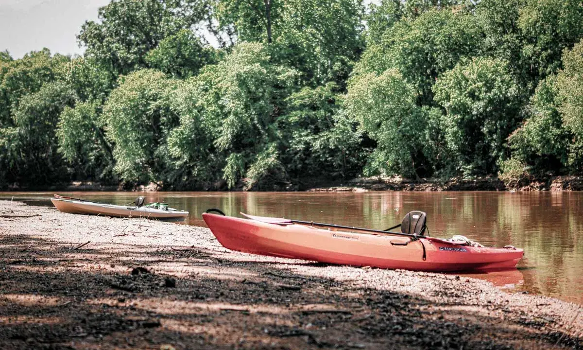 Dwa kajaki na brzegu rzeki na Podlasiu, otoczone bujną zielenią drzew.