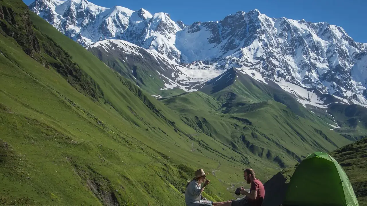Para odpoczywa po trekkingu w Gruzji, siedząc obok zielonego namiotu na tle majestatycznych, ośnieżonych gór.
