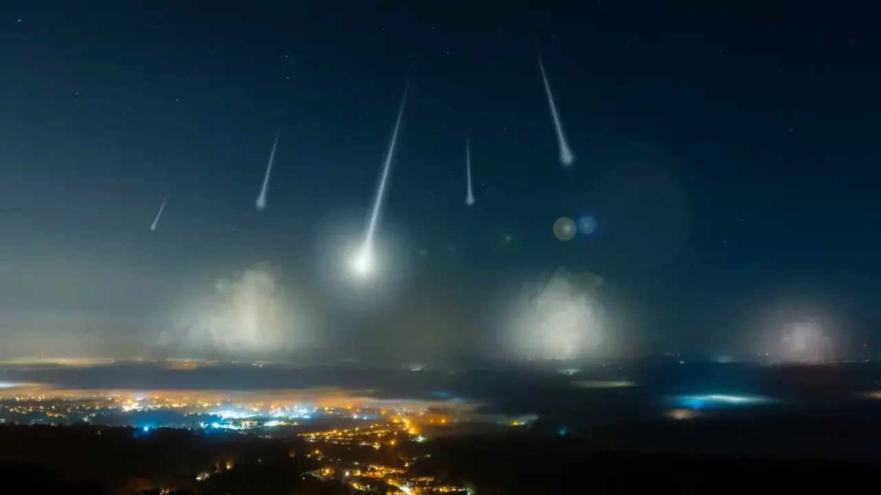 Noc perseidów nad miastem. Spadające gwiazdy przecinają ciemne niebo, oświetlając mgliste doliny i rozświetlone światłami zabudowania.