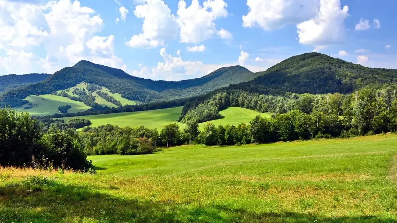 Zielone wzgórza i zalesione **beskid niski szczyty** pod błękitnym niebem z chmurami.