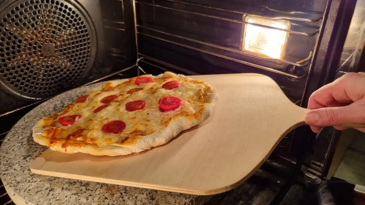 Pizza na kamieniu w piekarniku, gotowa do wyjęcia. Idealny sposób, jak piec pizzę na kamieniu dla chrupiącego spodu.