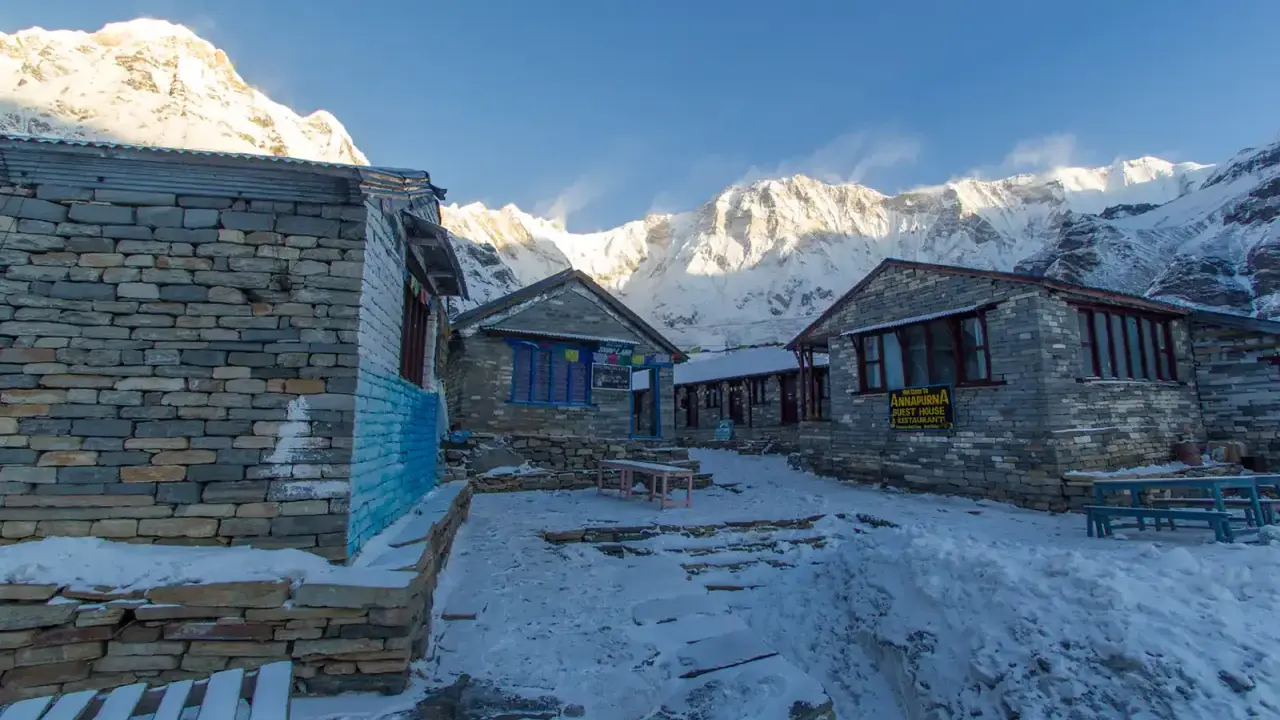 Kamienne budynki na trasie Annapurna Trekking, pokryte śniegiem, z majestatycznymi, ośnieżonymi szczytami w tle.