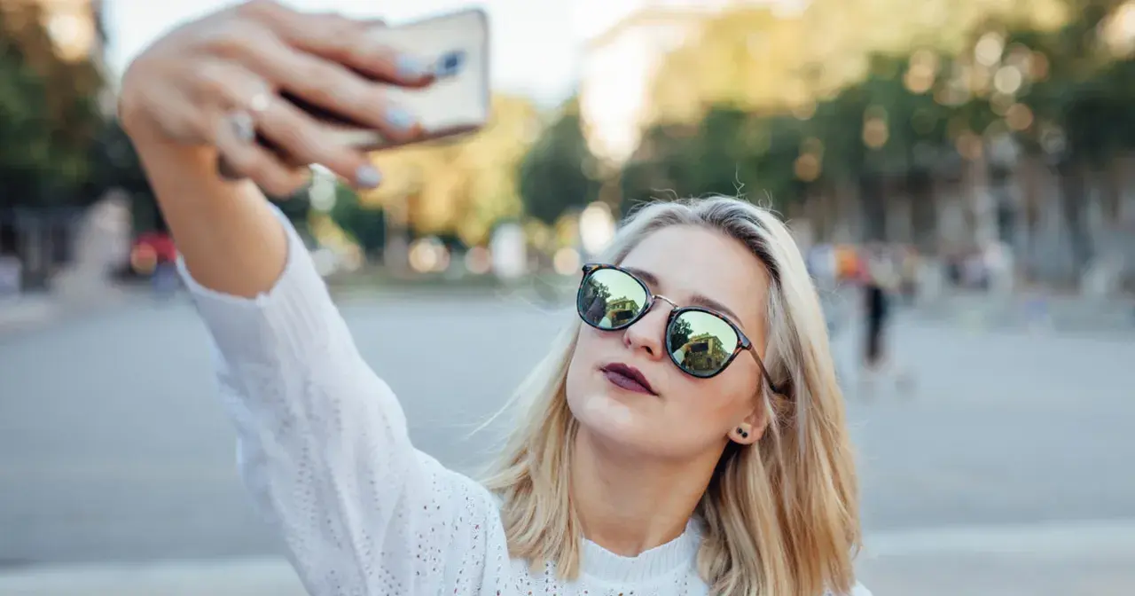 Blondynka w okularach robi sobie selfie, pokazując, jak zrobić dobre selfie.