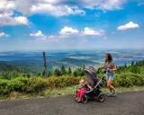 Mama z córką na spacerze, gdzie w góry z wózkiem. Piękny widok na dolinę i chmury.