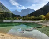 Jezioro w górach Słowenii z kamieniami w wodzie i ośnieżonymi szczytami w tle.