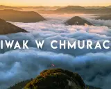 Widok z gór podczas trekkingu w Austrii. Chmury otulają szczyty, a na jednym z nich powiewa flaga.