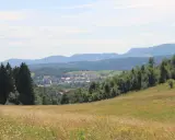 Widok na wieś u podnóża gór. W oddali widać zabudowania, a na pierwszym planie łąkę. Idealne miejsce na najkrótszy szlak na Chełmiec.