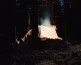 Nocne schronienie w lesie. Jasny namiot oświetla śnieżny krajobraz, tworząc przytulną atmosferę. Idealne miejsce, by zanocuj w lesie.