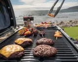 Co to jest grill? To idealne miejsce na letnie spotkania! Na ruszcie burgery, szaszłyki z mięsem i warzywami, a nad nimi krewetki. W tle morze i plaża.