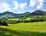 Zielone wzgórza i zalesione **beskid niski szczyty** pod błękitnym niebem z chmurami.