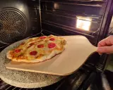 Pizza na kamieniu w piekarniku, gotowa do wyjęcia. Idealny sposób, jak piec pizzę na kamieniu dla chrupiącego spodu.