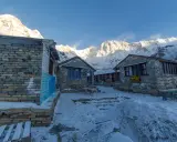 Kamienne budynki na trasie Annapurna Trekking, pokryte śniegiem, z majestatycznymi, ośnieżonymi szczytami w tle.