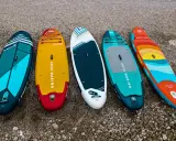 Pięć desek SUP leży na plaży. Zastanawiasz się, **deska sup jaką wybrać**? Wybierz swoją idealną!