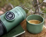 Zielona kawa w górach. Nanopresso i kubek z aromatycznym espresso na drewnianym pniu, wśród gałązek. Idealny towarzysz podróży.