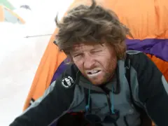Zmęczony alpinista z białym proszkiem na ustach, być może lek na chorobę wysokościową, w namiocie na tle śniegu.