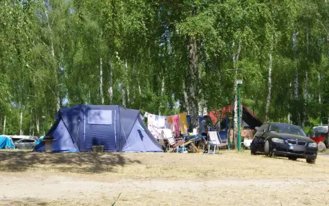 Idealne miejsce, gdzie pod namiot nad jezioro. W tle las, a przed namiotem rozłożone krzesła i suszące się pranie.