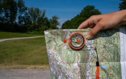 Dłoń trzyma mapę i kompas, pokazując, jak działa kompas w terenie.