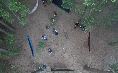 Ludzie rozbijają obóz w lesie, stosując zasady "leave no trace". Widać hamaki, plecaki i namiot.
