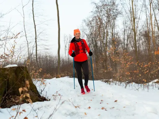 Kobieta w lesie zimą, ćwicząca nordic walking. Końcówki do kijków nordic walking zapewniają stabilność na śniegu.