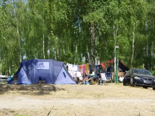 Idealne miejsce, gdzie pod namiot nad jezioro. W tle las, a przed namiotem rozłożone krzesła i suszące się pranie.