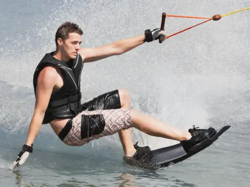 Młody mężczyzna na desce, ciągnięty przez linę, pokazuje, **wakeboarding co to** jest – sport wodny pełen adrenaliny i zabawy.
