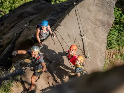 Grupa uśmiechniętych ludzi na via ferracie w Czechach. Wspinają się po skalnej ścianie, zabezpieczeni linami i kaskami.