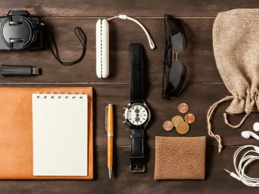 Zestaw EDC: aparat, pendrive, notes, długopis, zegarek, okulary, monety, portfel, słuchawki i woreczek.