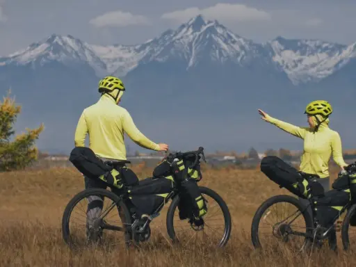 Para szykuje się na przygodę bike packing. W tle majestatyczne, ośnieżone góry.