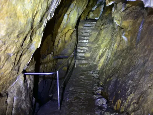 Kamienne schody prowadzą w głąb jaskini. Metalowa poręcz ułatwia przejście przez wilgotne, skalne korytarze.