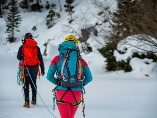 Dwóch alpinistów w zimowym krajobrazie, z plecakami i sprzętem, gotowych na wyprawę. To ich lista rzeczy na wyjazd w góry zimą.