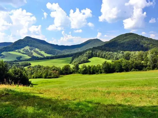 Zielone wzgórza i zalesione **beskid niski szczyty** pod błękitnym niebem z chmurami.