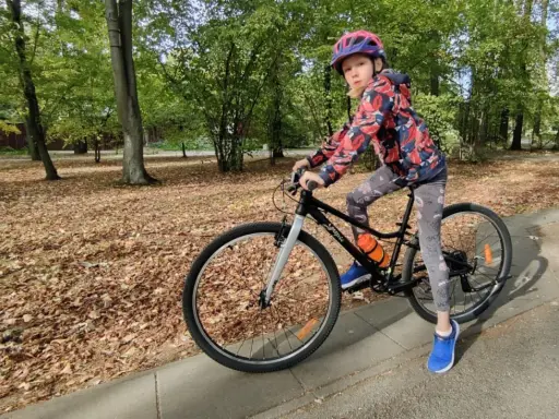 Dziewczynka na rowerze, idealny rozmiar roweru dla 10 latka. Jesienny park, liście na ziemi.