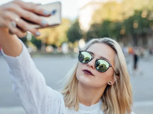 Blondynka w okularach robi sobie selfie, pokazując, jak zrobić dobre selfie.