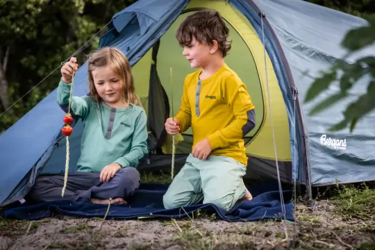 Dzieci w namiocie, ubrane w odzież Bergans, jedną z popularnych skandynawskich marek odzieżowych, jedzą truskawki.