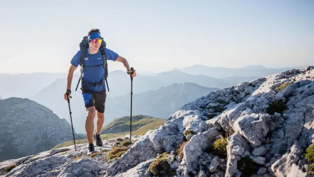 Mężczyzna w sportowym stroju z plecakiem i kijkami przemierza skalisty górski szlak. To esencja tego, co to trekking – pokonywanie trudnych terenów z pasją.