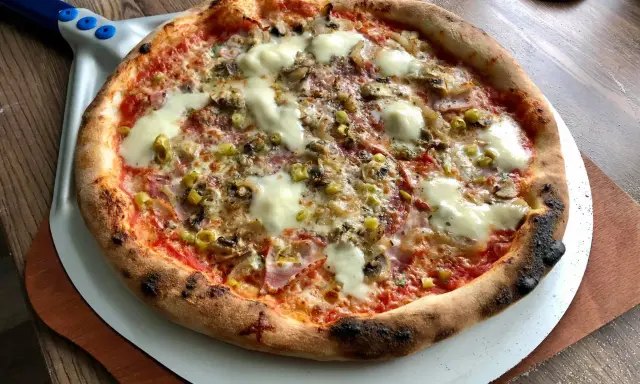 Pyszna pizza na kamieniu, z ciągnącym się serem, pieczarkami i oliwkami, gotowa do podania.