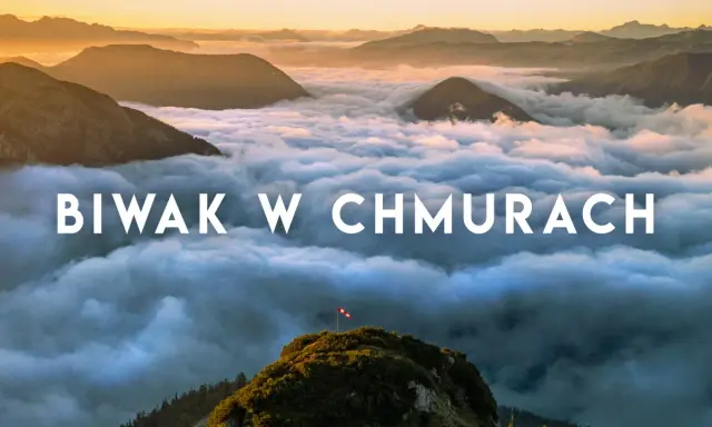 Widok z gór podczas trekkingu w Austrii. Chmury otulają szczyty, a na jednym z nich powiewa flaga.