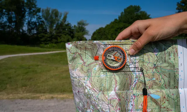 Dłoń trzyma mapę i kompas, pokazując, jak działa kompas w terenie.