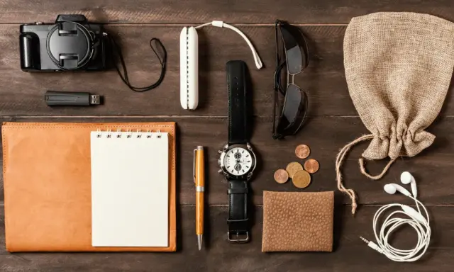 Zestaw EDC: aparat, pendrive, notes, długopis, zegarek, okulary, monety, portfel, słuchawki i woreczek.