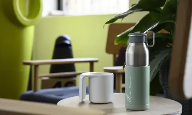 Zielony termos i biała filiżanka na stoliku. Idealny zestaw na wycieczkę w góry, by cieszyć się ciepłym napojem.