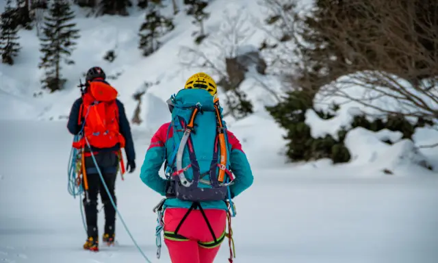 Dwóch alpinistów w zimowym krajobrazie, z plecakami i sprzętem, gotowych na wyprawę. To ich lista rzeczy na wyjazd w góry zimą.