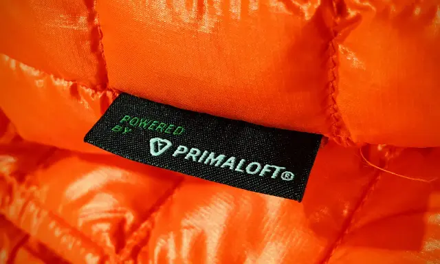 Pomarańczowa, pikowana tkanina z metką "Powered by Primaloft". To materiał izolacyjny, który zapewnia ciepło i lekkość.