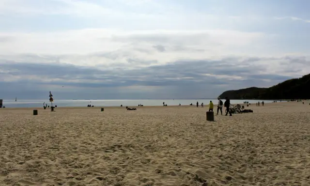 Plaża z ludźmi spacerującymi i odpoczywającymi. Idealny pomysł na weekend nad morzem.