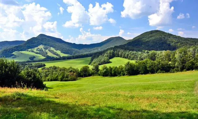 Zielone wzgórza i zalesione **beskid niski szczyty** pod błękitnym niebem z chmurami.