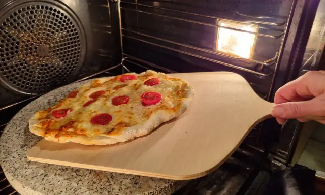 Pizza na kamieniu w piekarniku, gotowa do wyjęcia. Idealny sposób, jak piec pizzę na kamieniu dla chrupiącego spodu.
