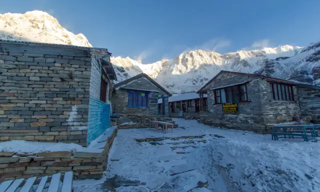 Kamienne budynki na trasie Annapurna Trekking, pokryte śniegiem, z majestatycznymi, ośnieżonymi szczytami w tle.