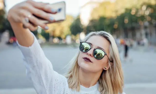 Blondynka w okularach robi sobie selfie, pokazując, jak zrobić dobre selfie.