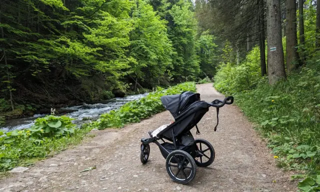 Spacer po górskim szlaku z wózkiem. Wózek stoi na ścieżce obok potoku i zielonego lasu.