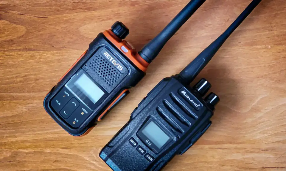 Dwa radiotelefony, jeden pomarańczowo-czarny RETC/IS, drugi czarny Midland G13, leżą na drewnianym blacie.